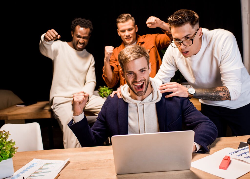 happy multicultural businesspeople showing winner gesture while working at night in office